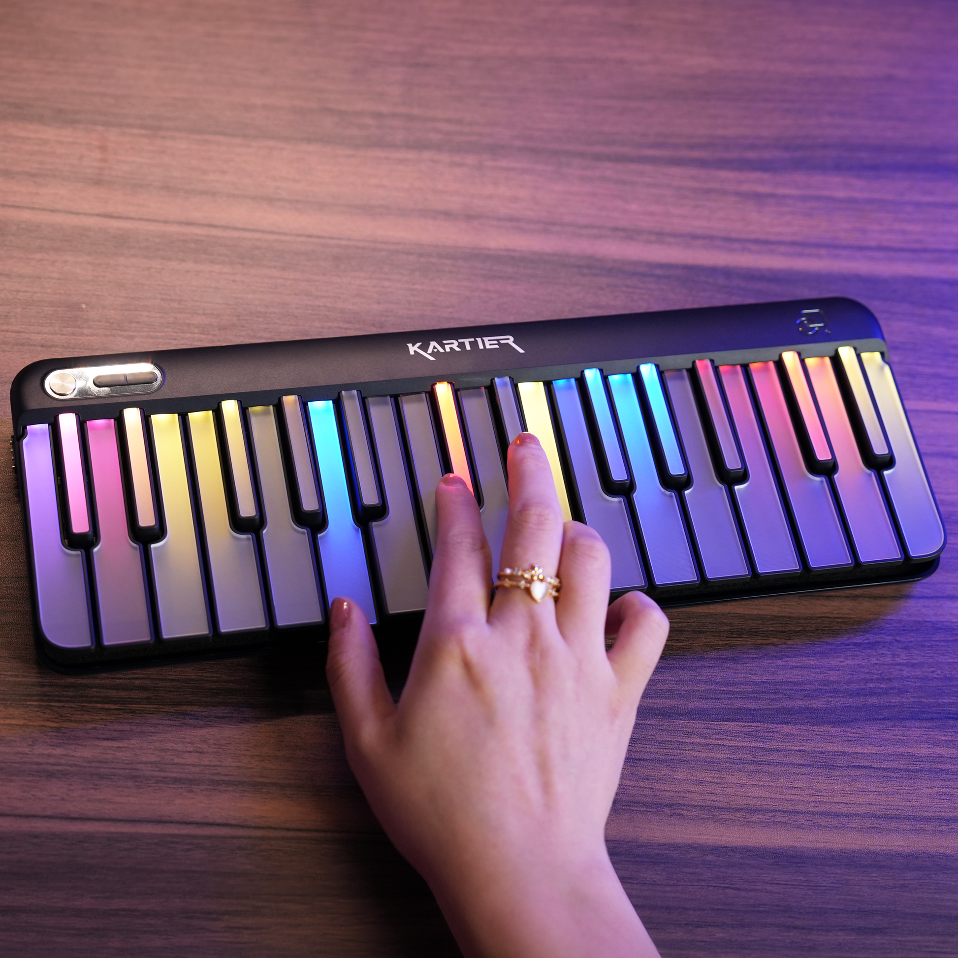 Kartier Piano Portable keyboard with colorful keys on a wooden surface, hand playing it.